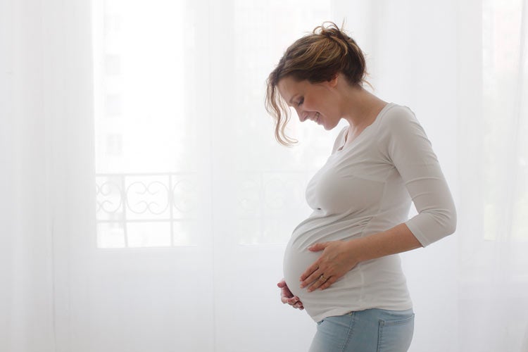 Pregnant woman standing in a room with white curtains